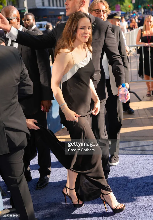 Rachel McAdams walking in a black dress and heels at an event.