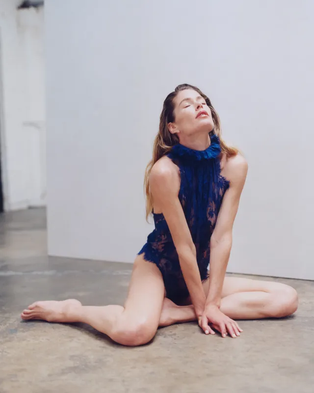Doutzen Kroes sitting barefoot on a studio floor in a navy outfit.