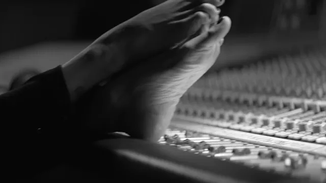 Penélope Cruz resting bare feet on a mixing desk in a monochrome scene.