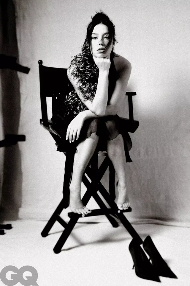 Adèle Exarchopoulos sitting in a tall chair in a monochrome portrait.