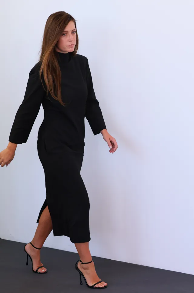 Adèle Exarchopoulos walking beside a pale wall in a black dress.