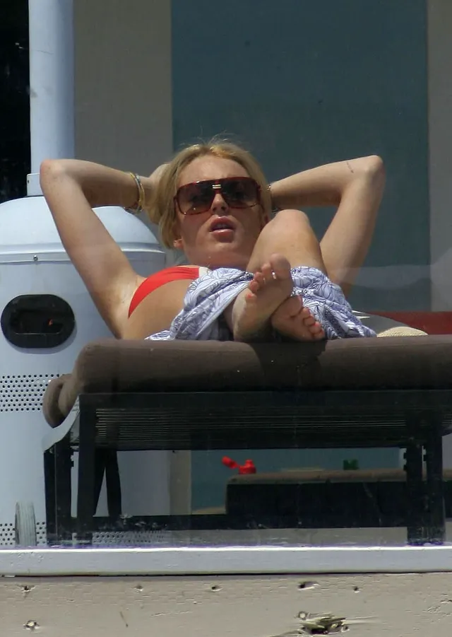 Lindsay Lohan reclining barefoot on a sun lounger in a red top.
