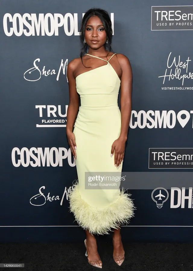 Carlacia Grant posing in a pale yellow dress and pointed heels on a carpet.