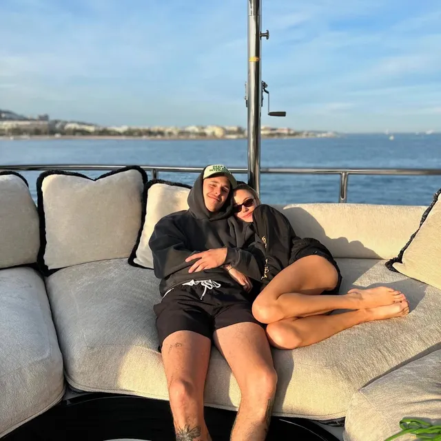 Maika Monroe reclining barefoot on a sofa with a companion.