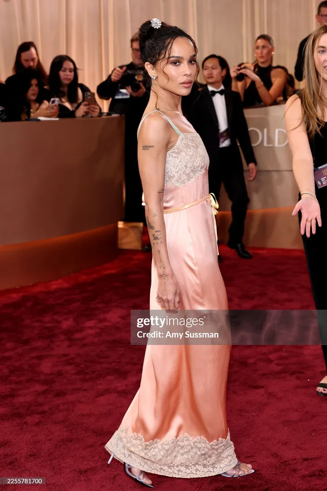 Zoë Kravitz turning toward cameras in a pale pink dress.