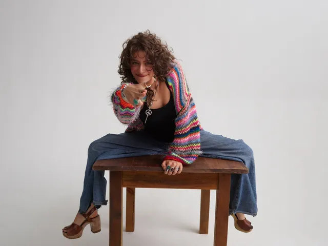 Odessa A'zion sitting on a table in jeans and brown heels.