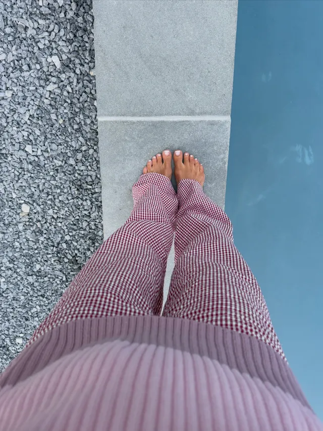 Nina Agdal showing her bare toes beneath a pink knit outfit beside a pool.
