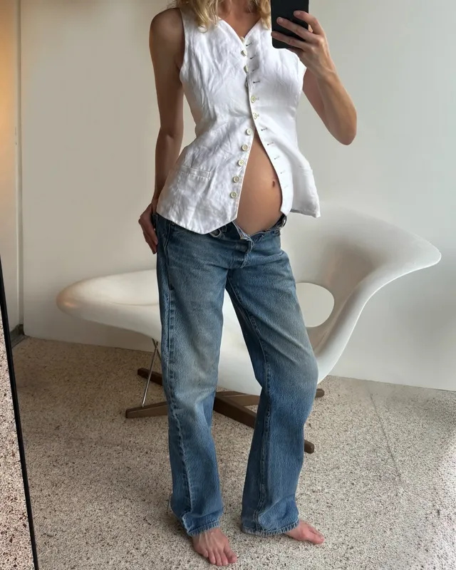Elsa Hosk taking a barefoot mirror photograph in jeans and a white blouse.