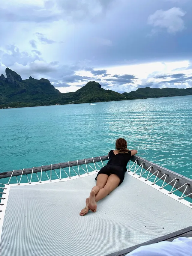 Halle Berry reclining barefoot on a net over the water.