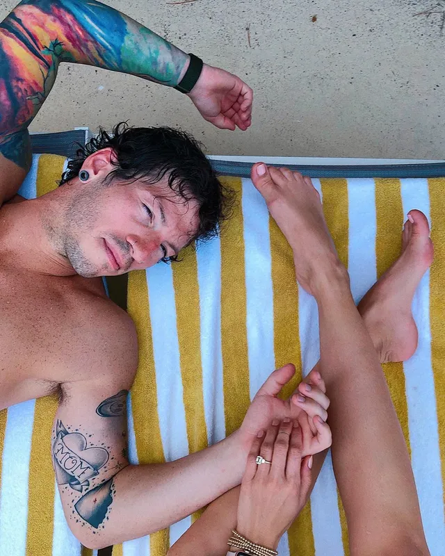Debby Ryan resting on a striped lounger beside another person.