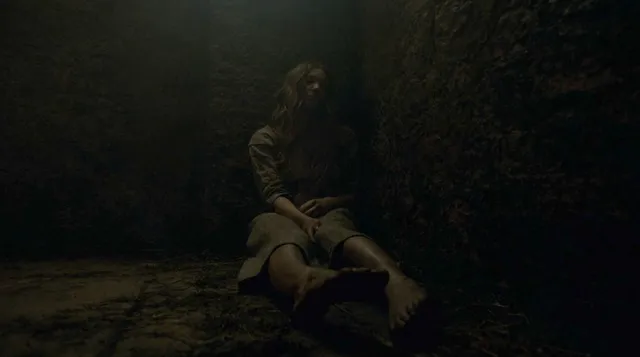 Natalie Dormer sitting on stone steps in a dark screen scene.