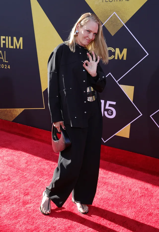 Uma Thurman wearing a black outfit and heels on a red carpet.