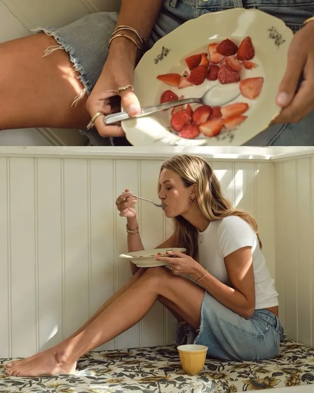 Josephine Skriver sitting barefoot on a kitchen counter while eating fruit.