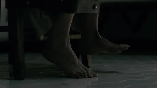 Eva Green standing barefoot on a tiled floor in a dark film scene.