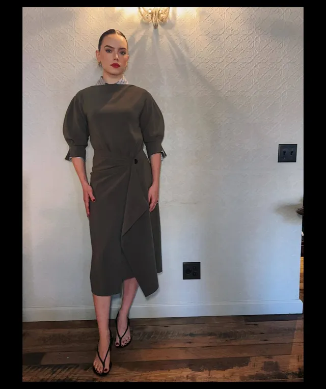 Daisy Ridley posing indoors in a dark green dress.