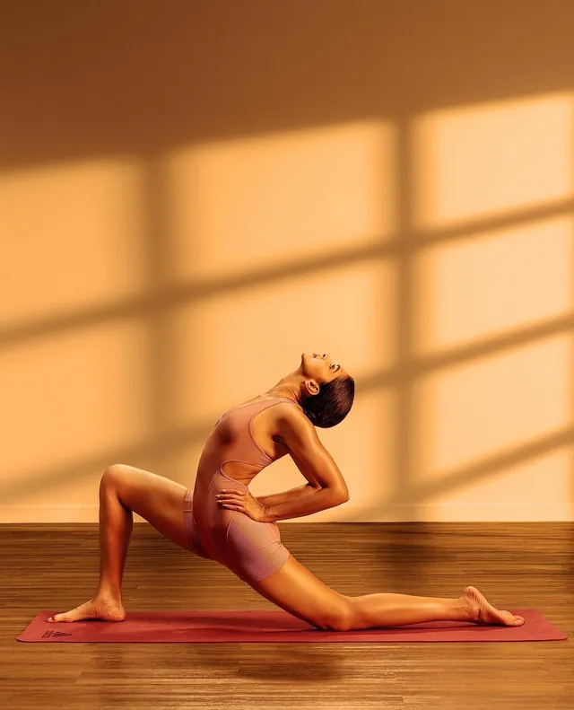Deepika Padukone stretching barefoot on a yoga mat in warm studio light.