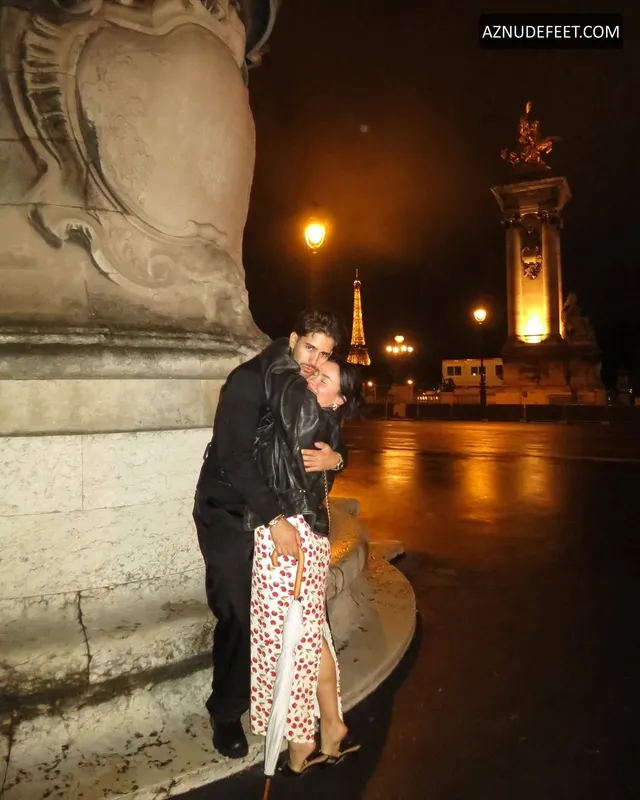 Cierra Ramirez in a patterned skirt and heeled sandals beside a stone fountain at night.