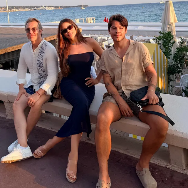 Sofía Vergara sitting between two people in a dark outfit and clear heels.