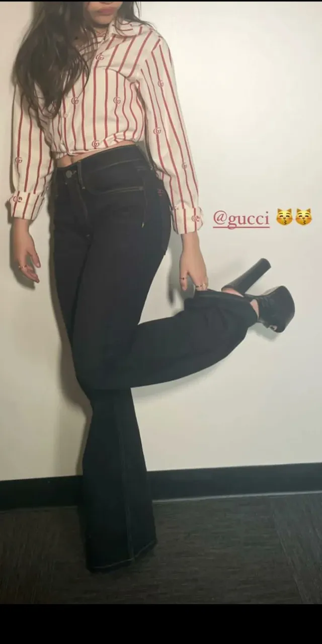 Ariana Greenblatt standing indoors in a striped top and black heels.