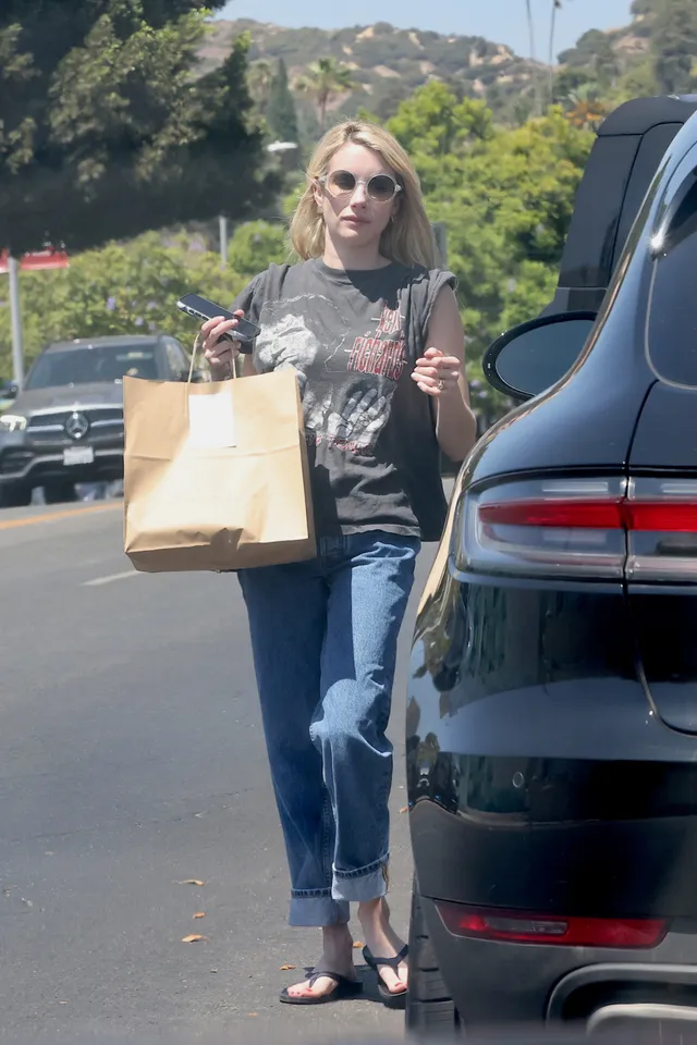Emma Roberts standing beside a car in jeans and black heeled sandals.