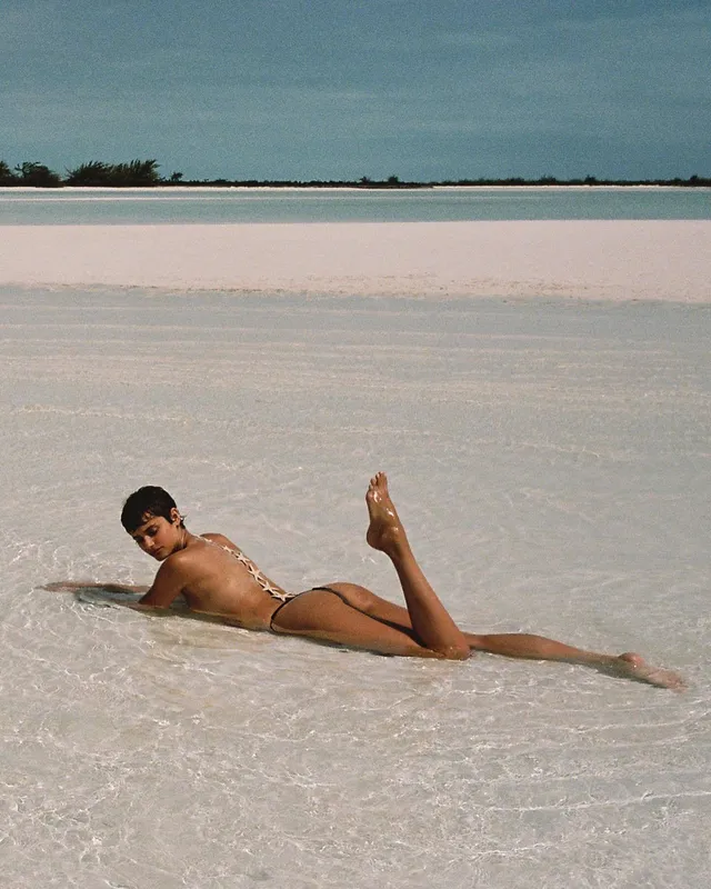 Taylor Hill lying barefoot in shallow beach water.