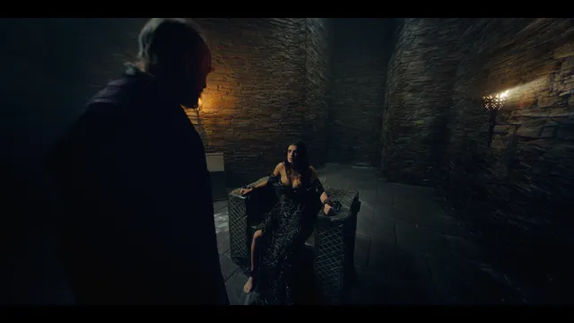 Anya Chalotra sitting opposite a man in a dimly lit film scene.