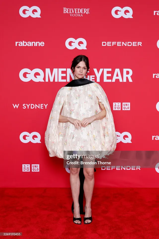 Maia Mitchell posing in a cape dress and black heels.