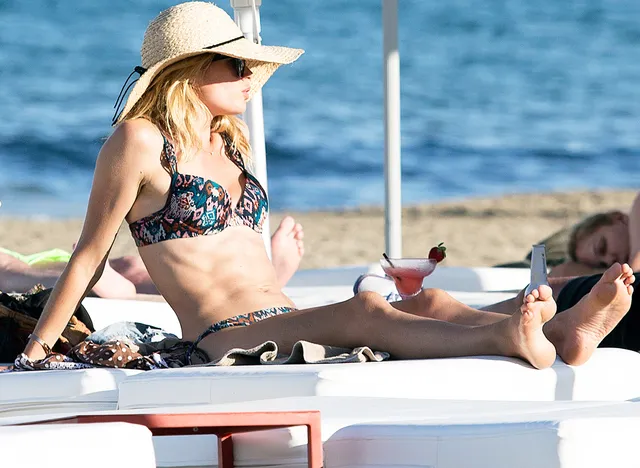 Doutzen Kroes reclining barefoot on a beach lounger in a sunhat.