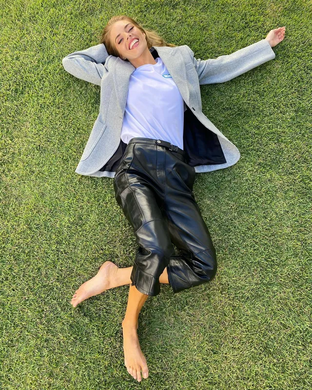 Samara Weaving lying barefoot on grass in a jacket and cropped trousers.