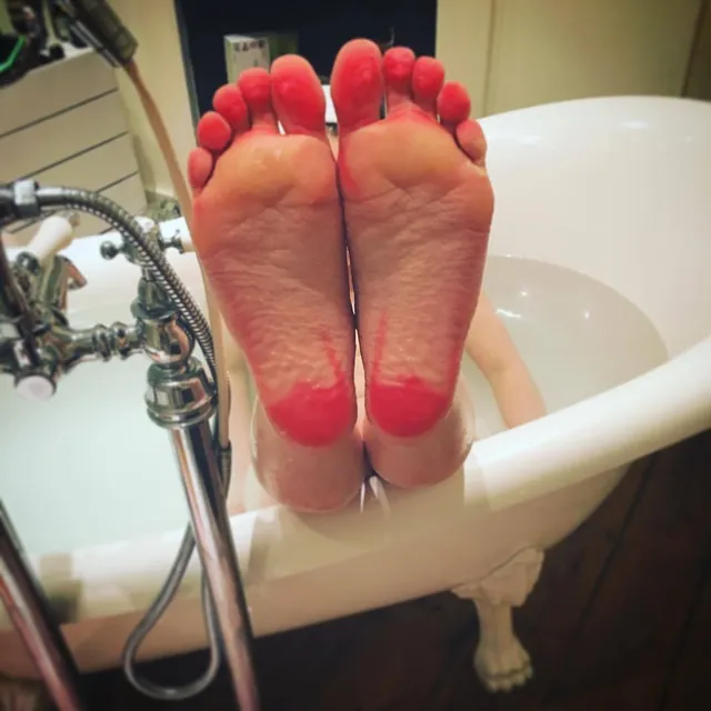Emilia Clarke with painted bare soles raised over a bathtub.
