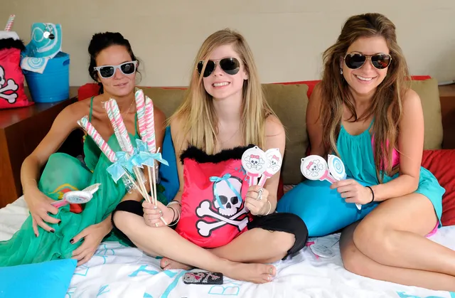 Avril Lavigne sitting cross-legged on a bed between two other people.