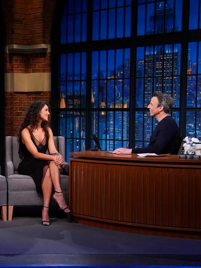 Eiza González sitting in a black dress and heels during an interview.