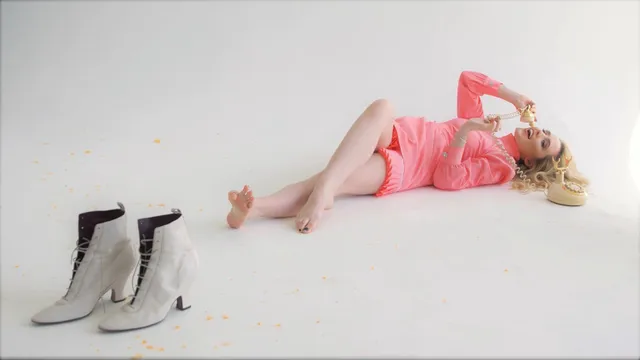 Kathryn Newton reclining barefoot in a pink dress beside a pair of boots.