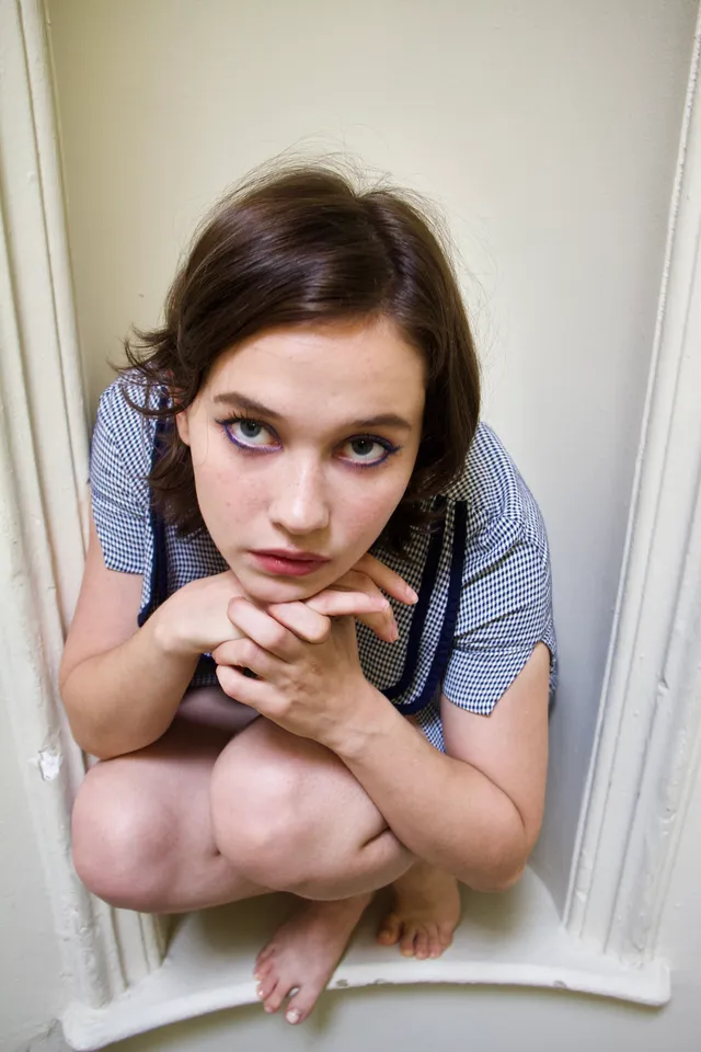 Cailee Spaeny crouching barefoot in a doorway for a portrait.