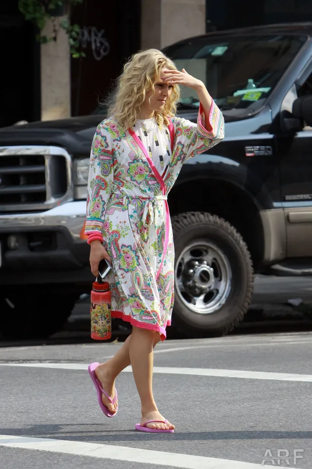 AnnaSophia Robb walking beside a vehicle in a patterned robe and flip-flops.