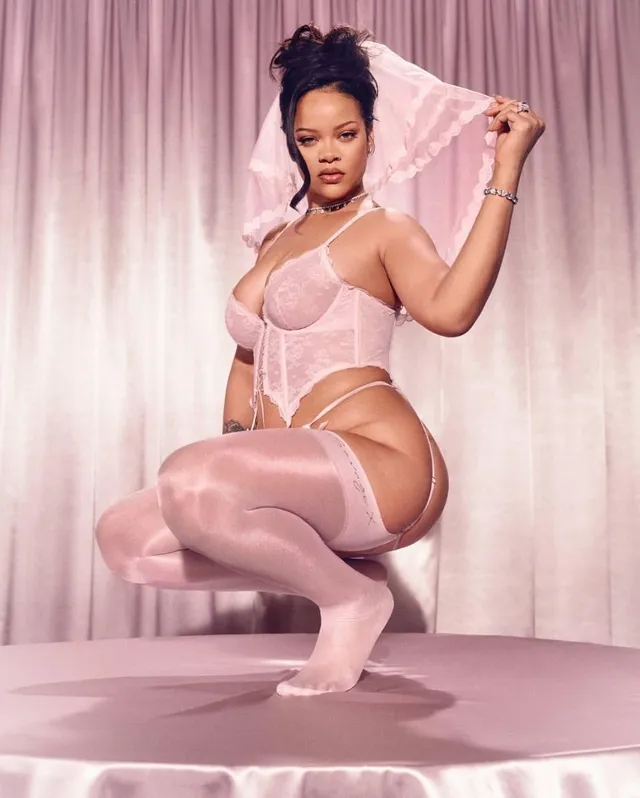 Rihanna crouching in a pink outfit and pink thigh-high stockings.