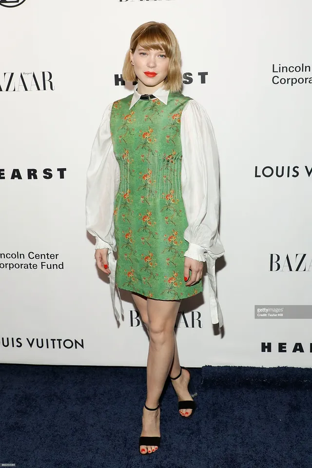 Léa Seydoux posing in a patterned green dress and black sandals.