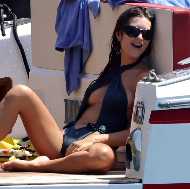 Emily Ratajkowski sitting barefoot aboard a boat in a dark swimsuit.