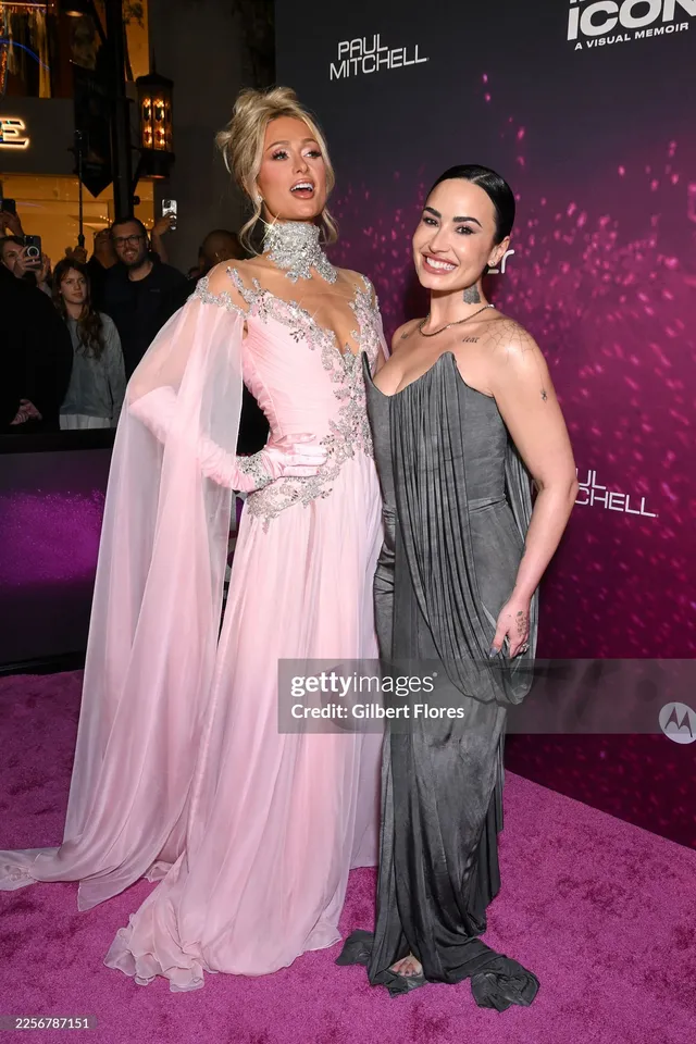 Demi Lovato standing beside another person in a grey gown and heels.