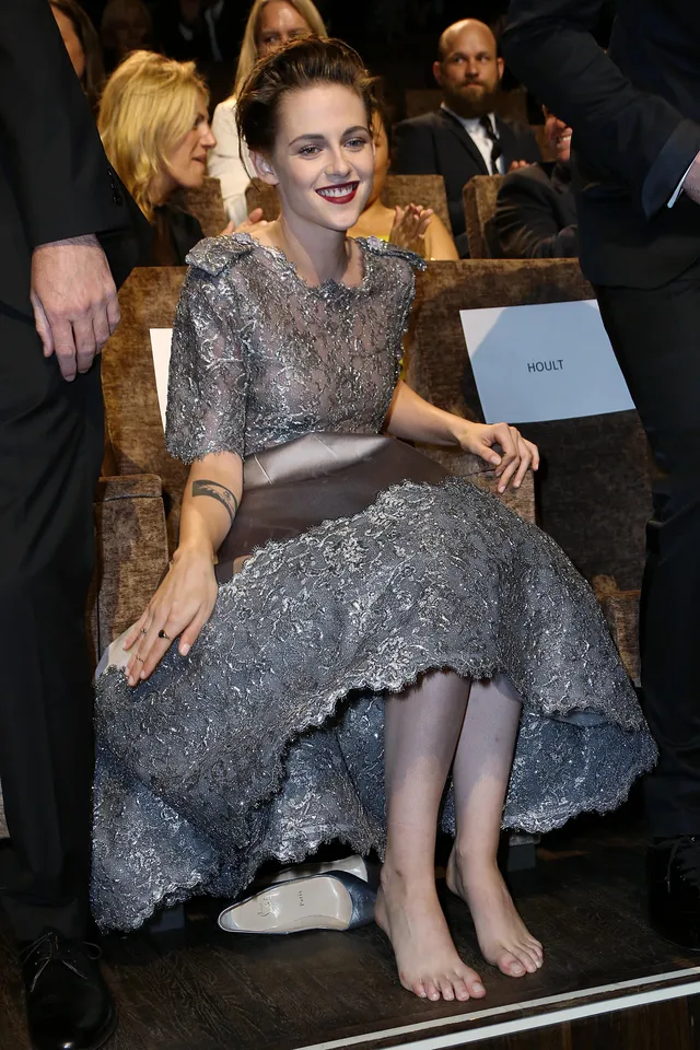 Kristen Stewart sitting barefoot beside other guests at an event.