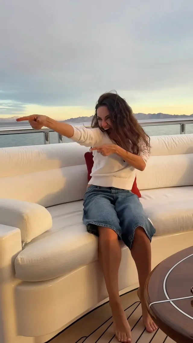 Mila Kunis sitting barefoot aboard a boat.