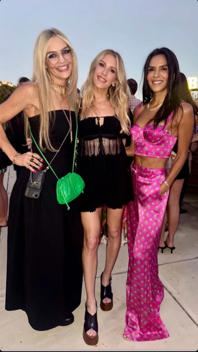 Ellie Goulding posing between other people in a black dress and heels.