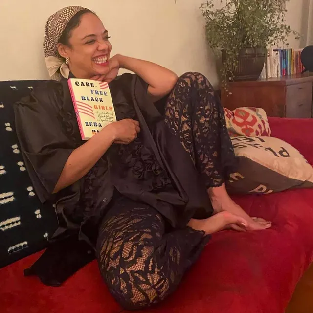 Tessa Thompson sitting on a red sofa holding a book.