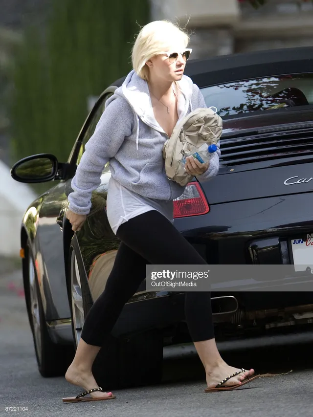 Elisha Cuthbert walking beside a car in black leggings and flat sandals.