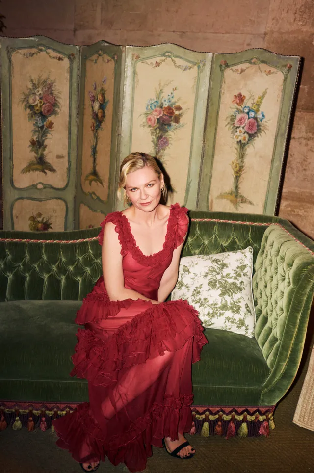 Kirsten Dunst sitting on a green sofa in a red dress.