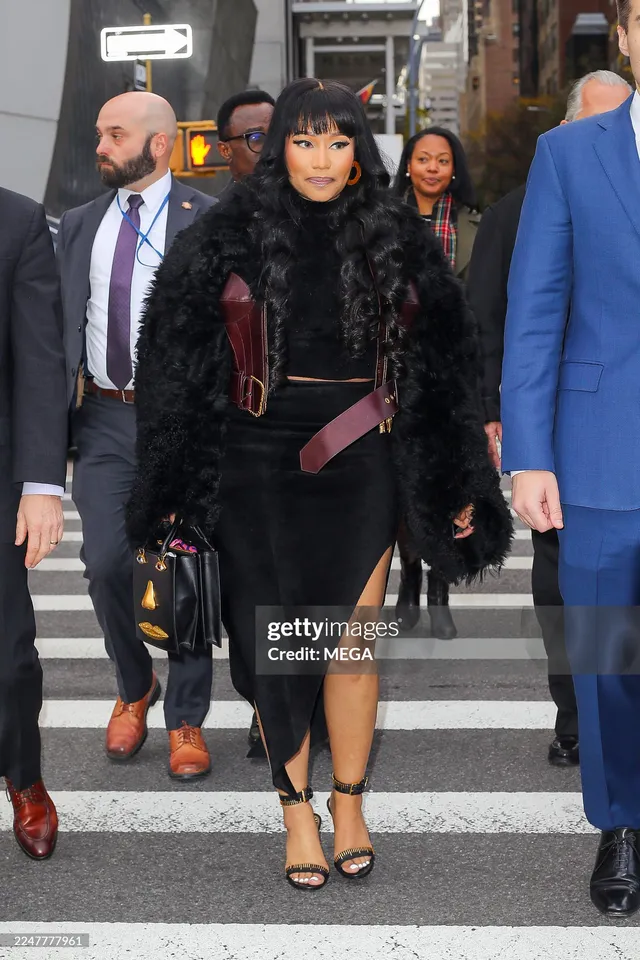 Nicki Minaj walking outdoors in a dark outfit and black heels.
