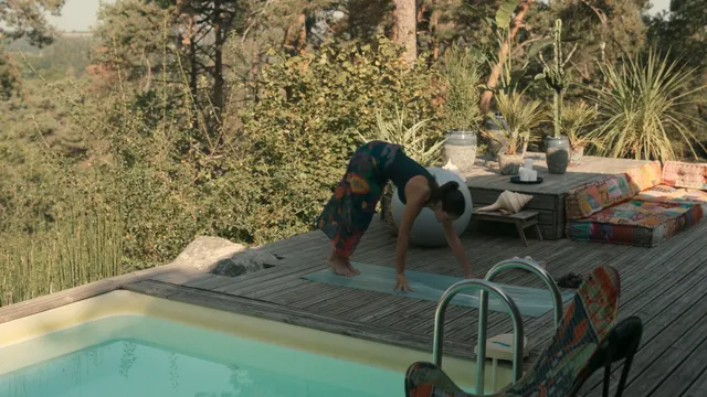 Adria Arjona moving barefoot across a poolside deck in a film scene.