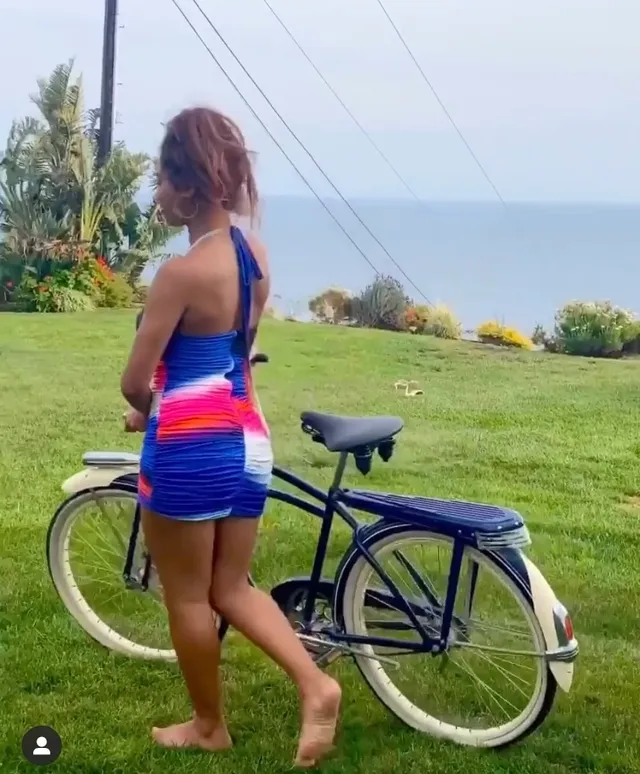 Sierra Capri posing barefoot by a bicycle on a lawn.