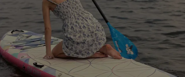 Anna Kendrick sitting barefoot on a paddleboard.