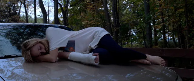 Maika Monroe lying barefoot outdoors in a scene.